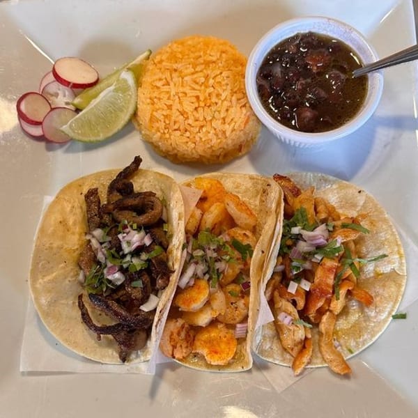 Three tacos with rice, black beans, radishes, and lime on a white plate.