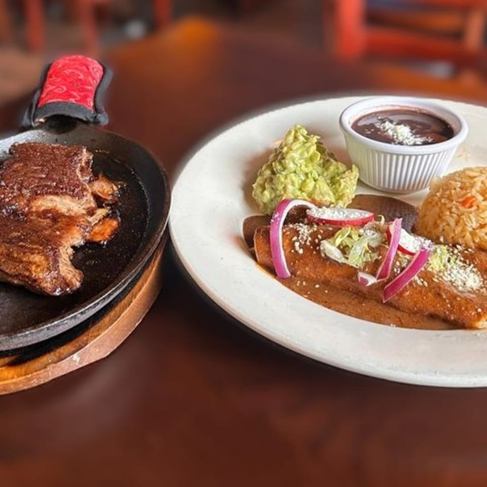 Sizzling steak fajitas and a plate of enchiladas with rice, guacamole, and black beans.
