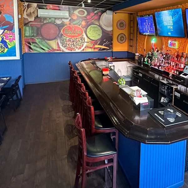 Vibrant Mexican restaurant interior with a long bar, dining tables, and colorful wall art.