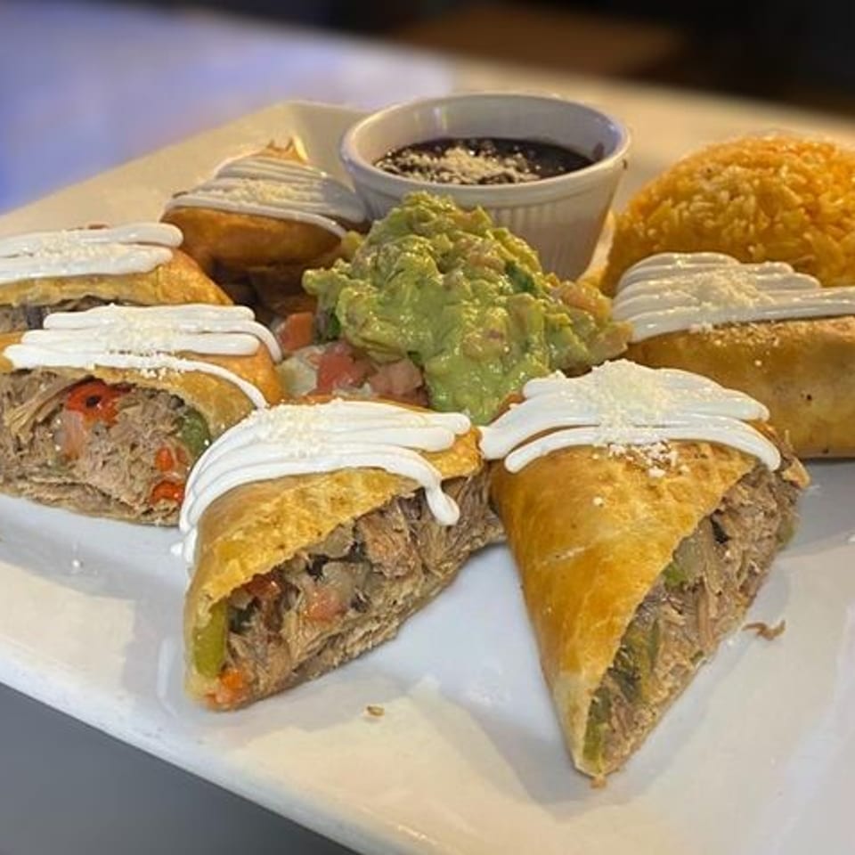 A white plate with several empanadas, guacamole, black beans, and yellow rice.