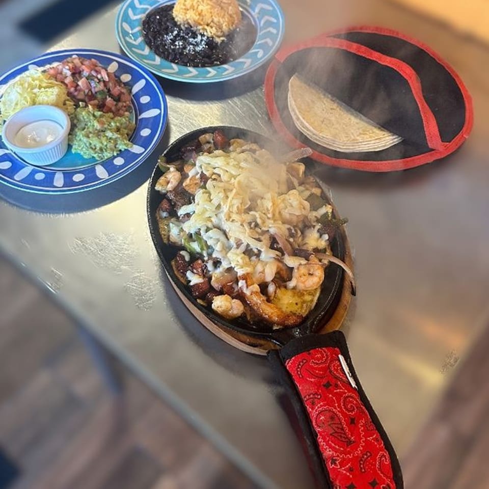 Sizzling fajitas with melted cheese, rice, beans, guacamole, pico de gallo, and warm tortillas.